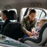Jak przewozić dziecko w taksówce? Mama zapina fotelik swojego dziecka na tylnym siedzeniu taksówki